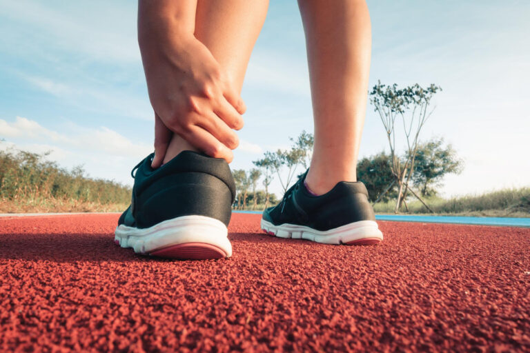 Close-up of a person adjusting their left ankle in black running shoes on a red outdoor track.